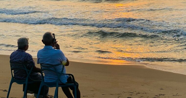 retired couple sitting at the beach, watching the sunset.