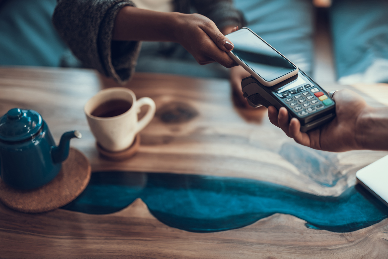 Close up of woman hand with manicure putting her smartphone to the credit card payment machine while using contactless system of payment in the cafe